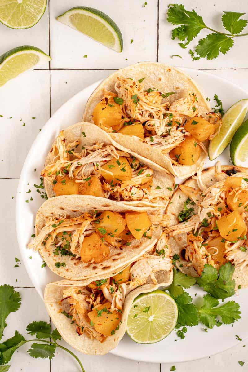 A plate with pineapple chicken tacos garnished with lime and cilantro.