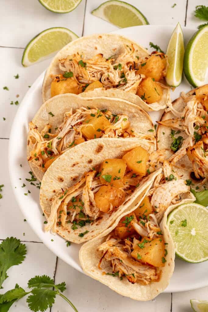 A plate with pineapple chicken tacos garnished with lime and cilantro.