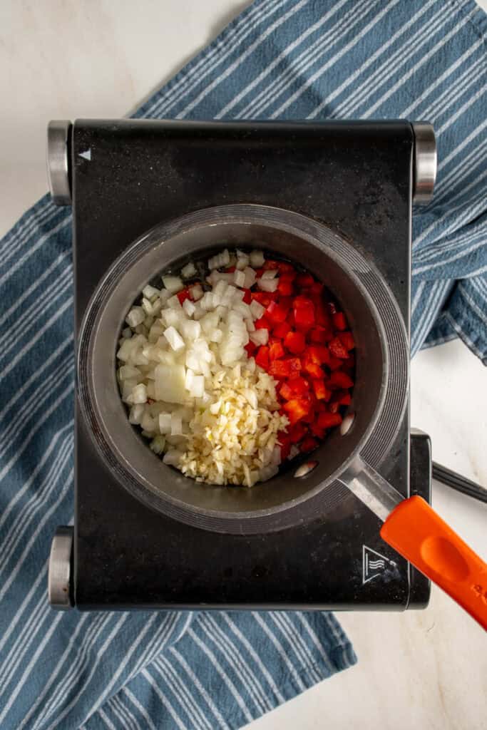 Fresh diced onions, red bell pepper, and garlic in a pot.