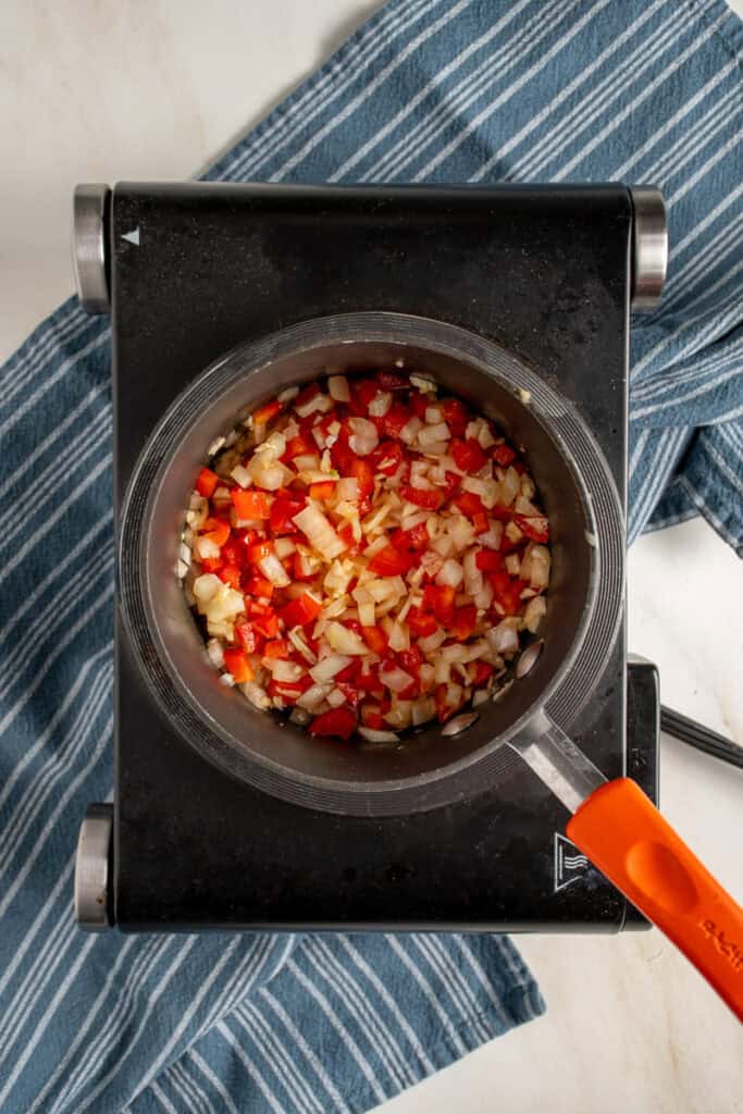 Red bell pepper and diced onion in a pot.