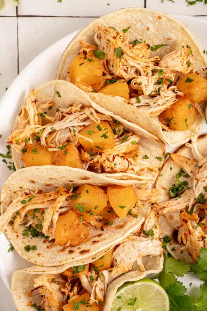 A plate with pineapple chicken tacos garnished with lime and cilantro.