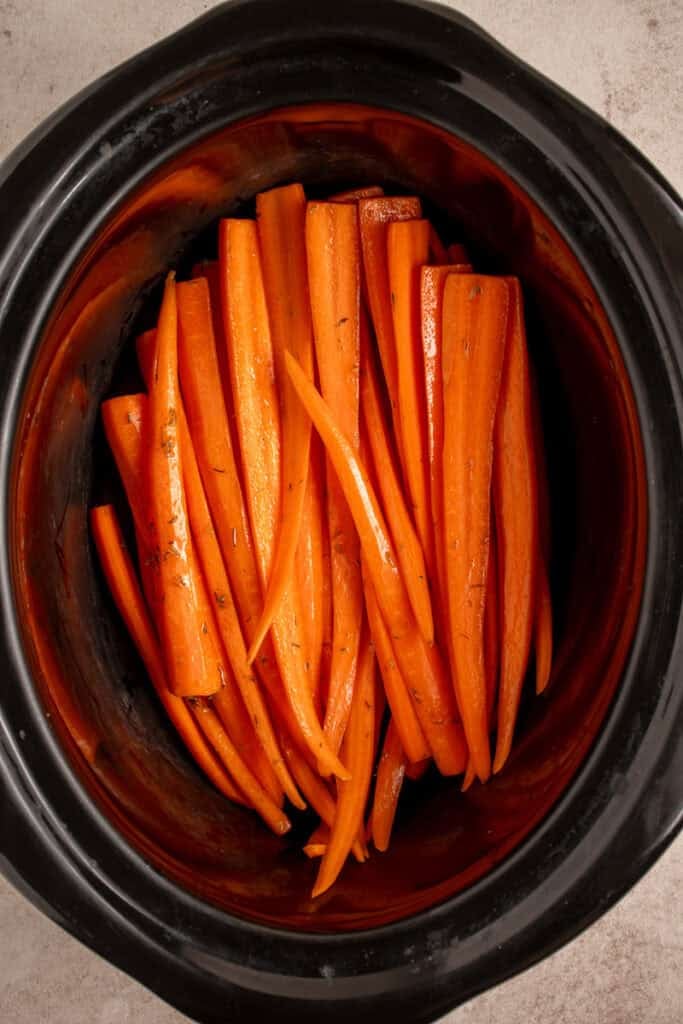 Raw carrots in a black crockpot.