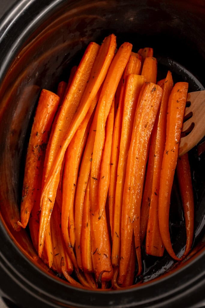A black crockpot with cooked carrots.