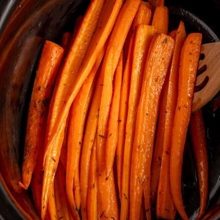 A black crockpot with cooked carrots.
