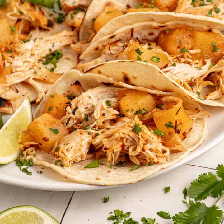 A plate with pineapple chicken tacos garnished with lime and cilantro.