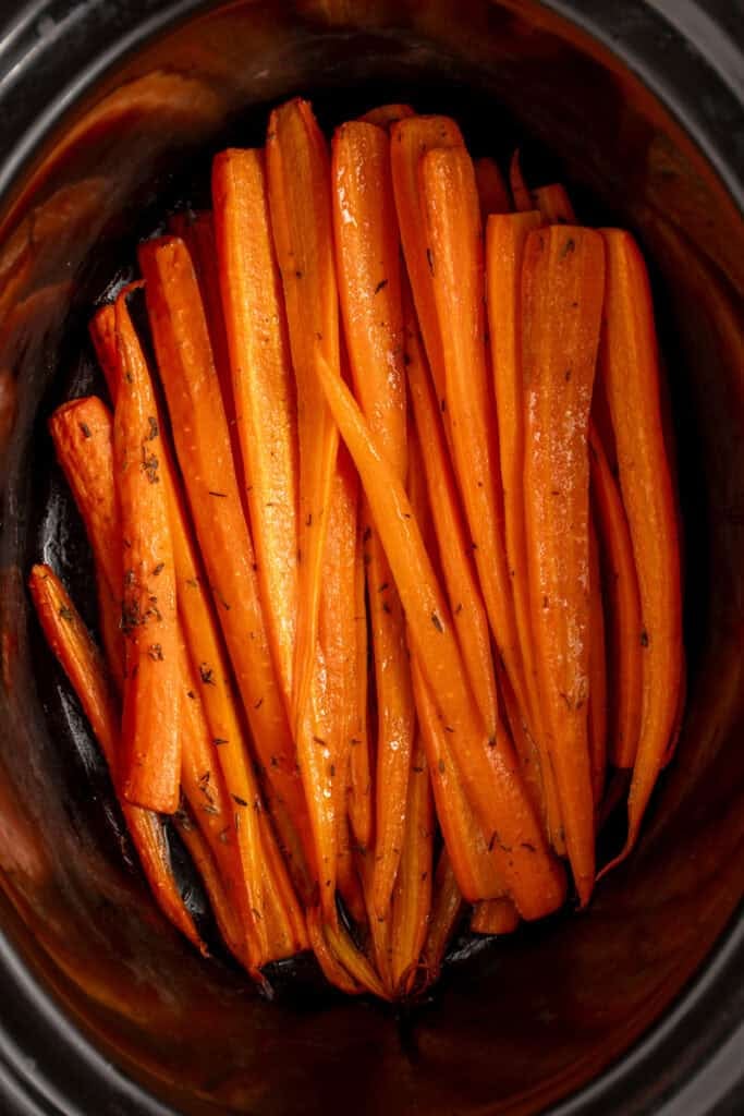 A black crockpot with cooked carrots.