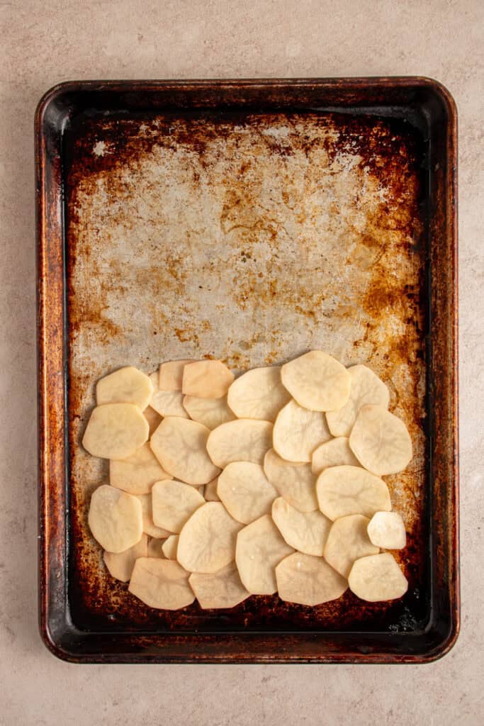 A sheet pan with layered sliced potatoes.