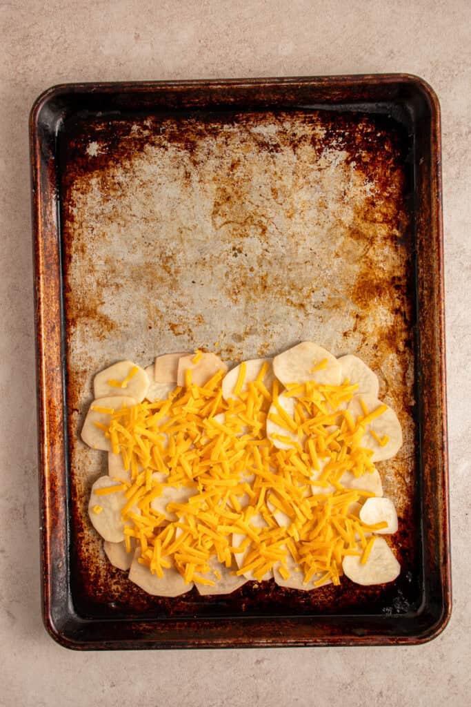 Sheet pan with a layer of potatoes and cheese.