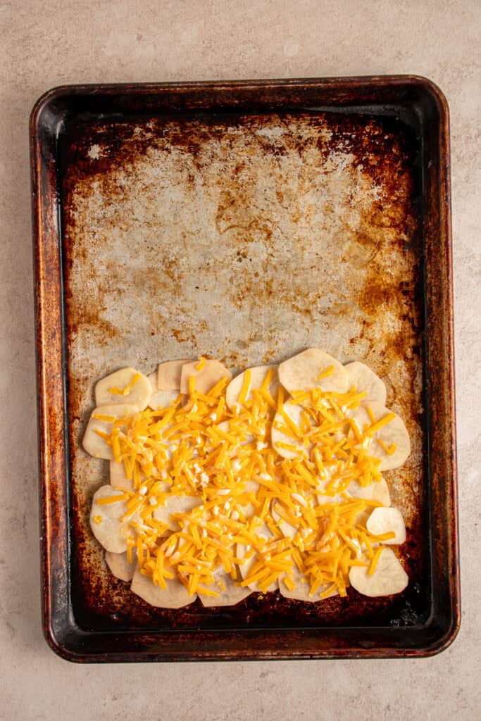A sheet pan with a layer of potatoes, cheese, and half and half mixture.
