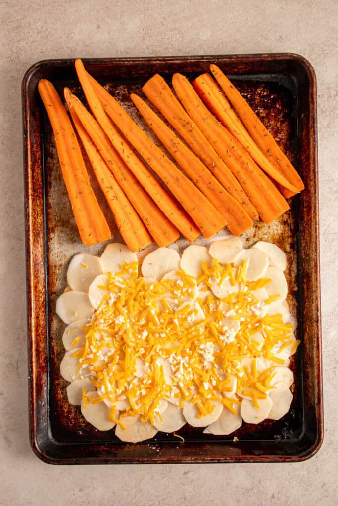 A sheet pan with prepared cheesy potatoes and carrots.