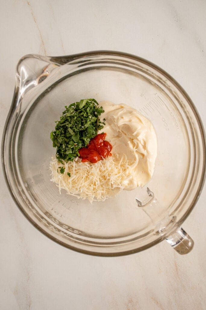 A bowl with mayo, parm cheese, cilantro, and sriracha.