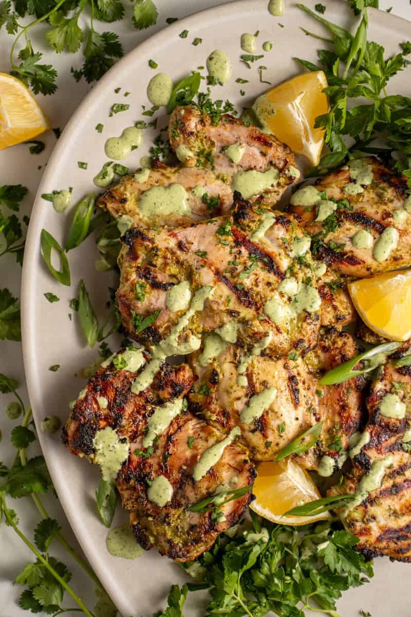 A platter of grilled green goddess chicken thighs with green goddess sauce and fresh herbs.