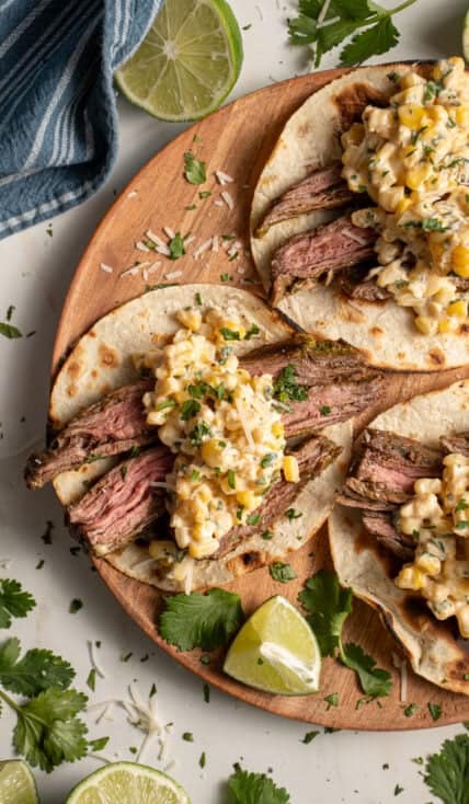 Steak and elote tacos laid out on a wood plate.