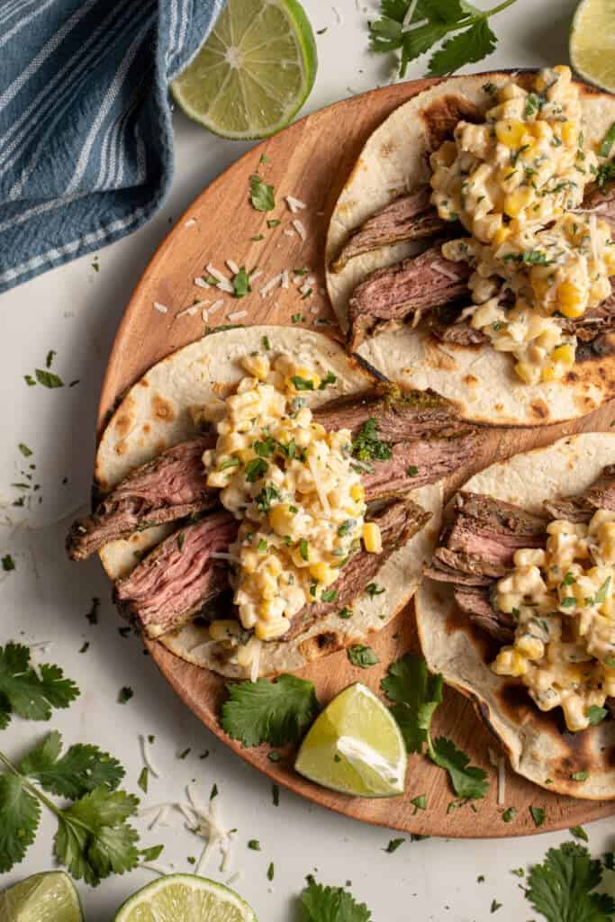 Steak and elote tacos laid out on a wood plate.