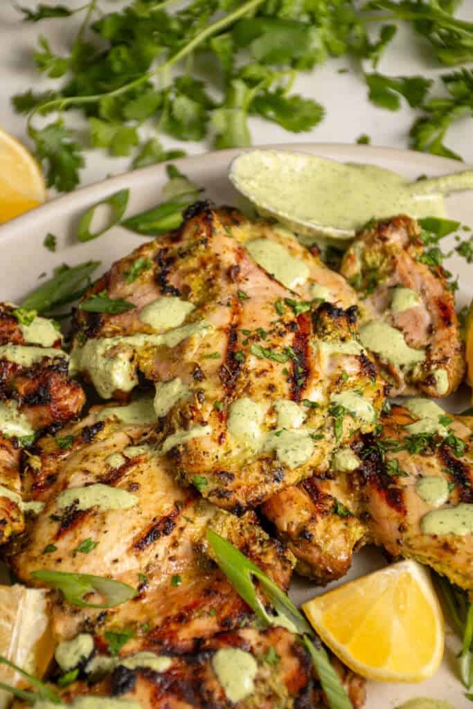 A platter of grilled green goddess chicken thighs with green goddess sauce and fresh herbs.