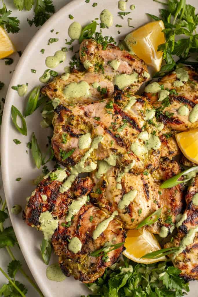 A platter of grilled green goddess chicken thighs with green goddess sauce and fresh herbs.
