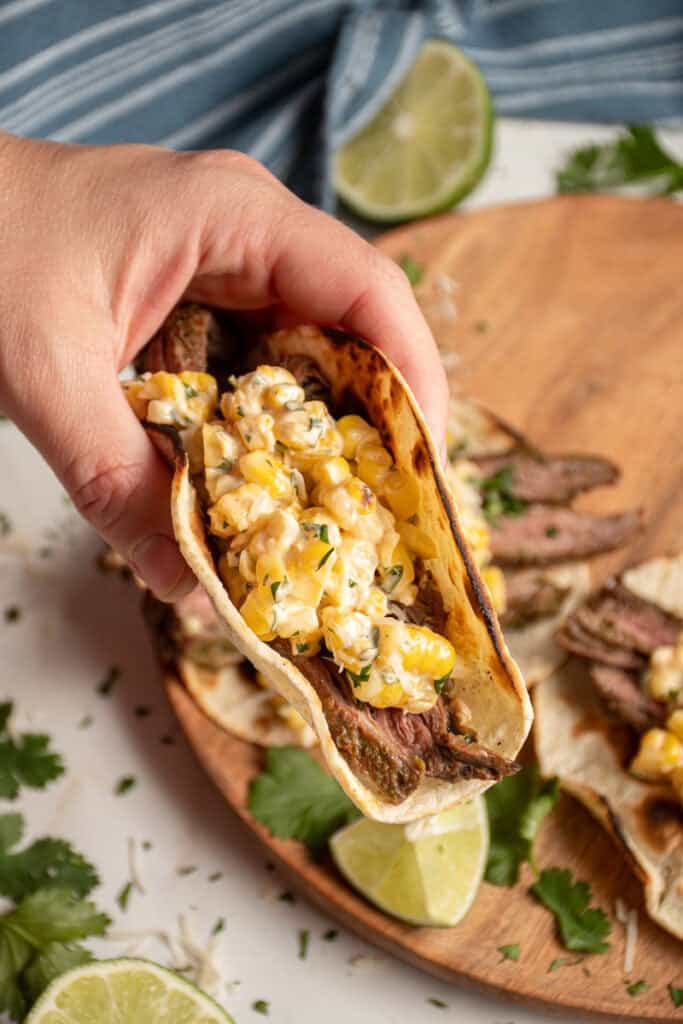A hand holding a steak and elote taco.