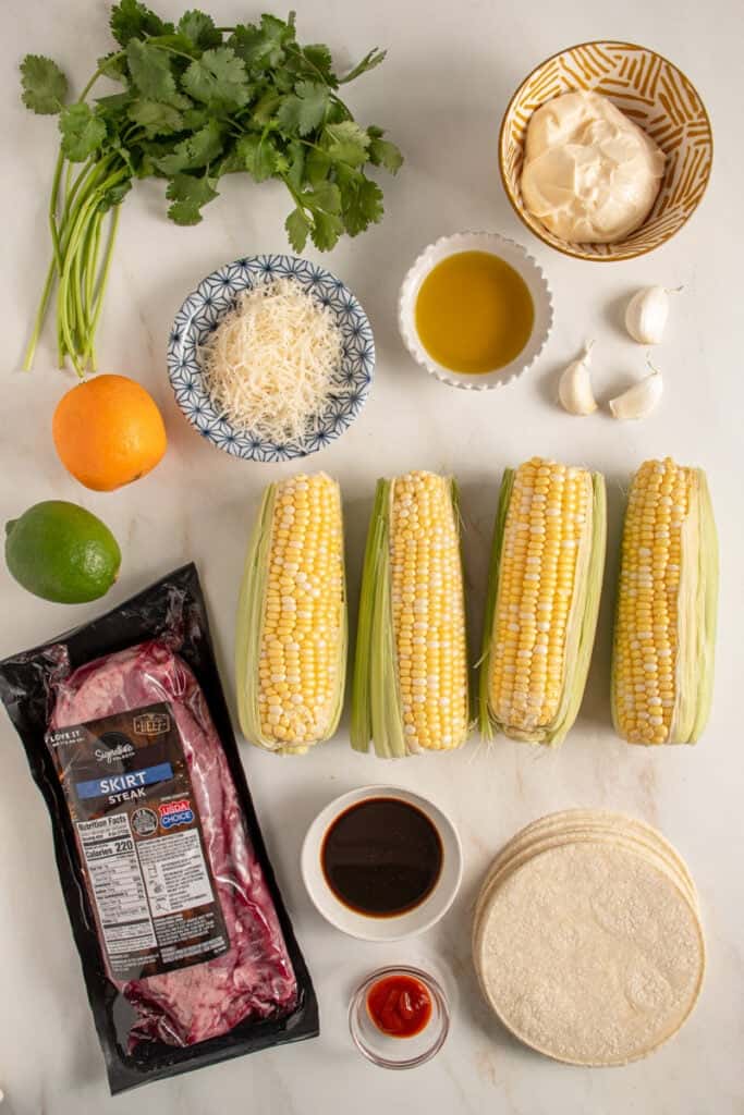 Ingredients for steak and elote tacos laid out on a tabletop.