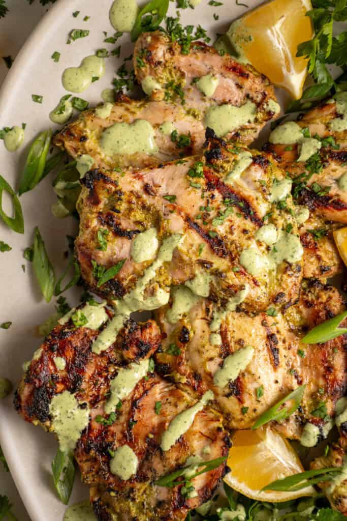 A platter of grilled green goddess chicken thighs with green goddess sauce and fresh herbs.