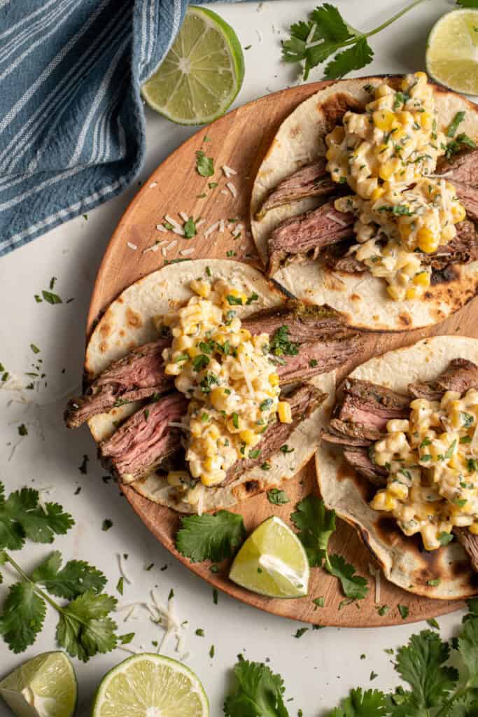 Steak and elote tacos laid out on a wood plate.