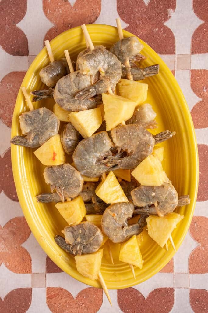 Raw shrimp and pineapple on skewers on a plate.
