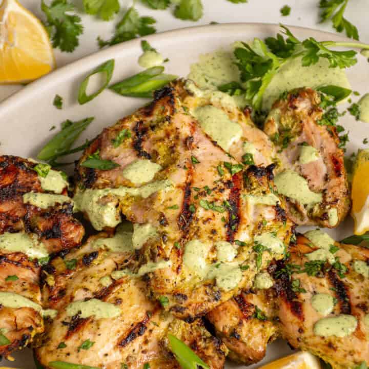 A platter of grilled green goddess chicken thighs with green goddess sauce and fresh herbs.