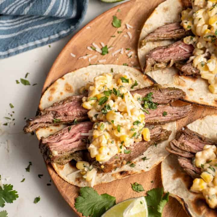 Steak and elote tacos laid out on a wood plate.