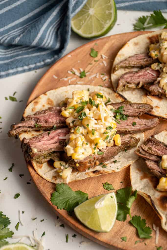Steak and elote tacos laid out on a wood plate.