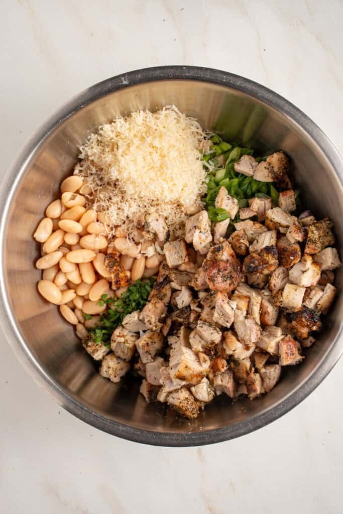 Adding chopped grilled chicken to the dense white bean salad.