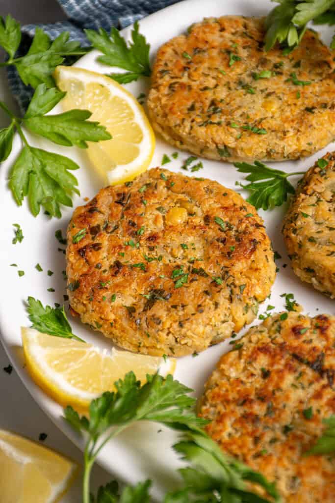 A plate with golden brown and crispy chickpea fritters, fresh parsley, and lemon slices.