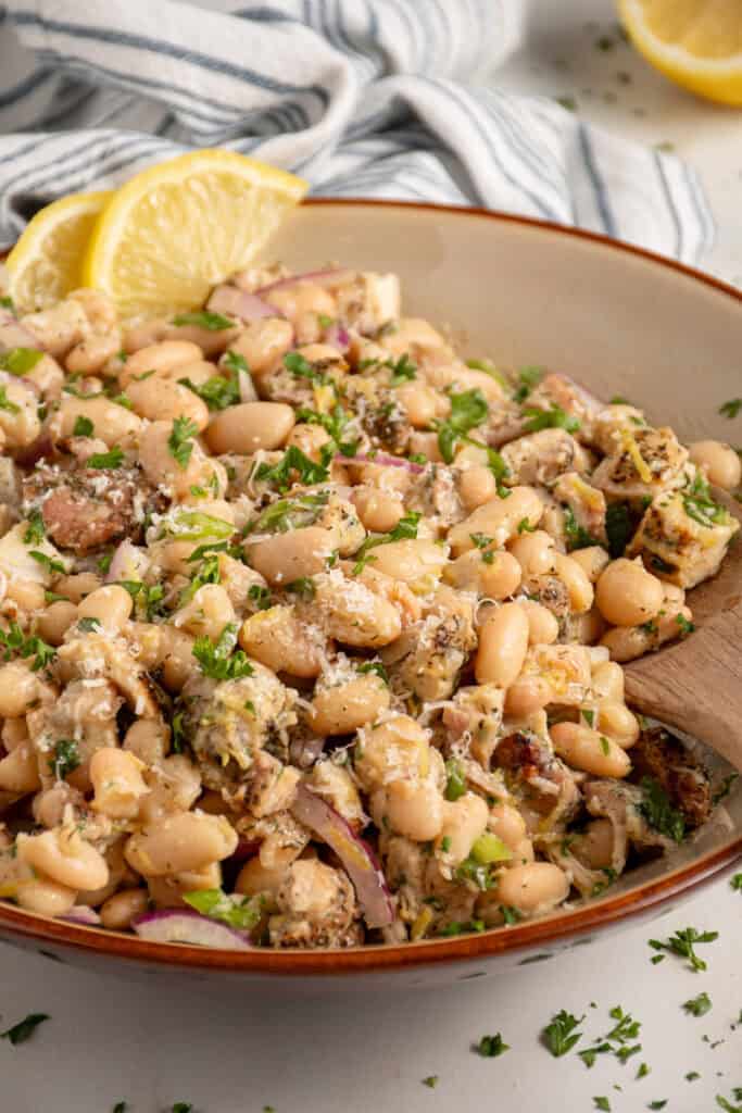 Bowl with dense white bean salad and grilled chicken garnished with parsley.
