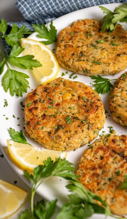 A plate with golden brown and crispy chickpea fritters, fresh parsley, and lemon slices.