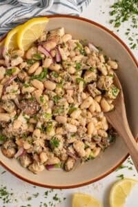 Bowl with dense white bean salad and grilled chicken garnished with parsley.