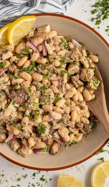 Bowl with dense white bean salad and grilled chicken garnished with parsley.