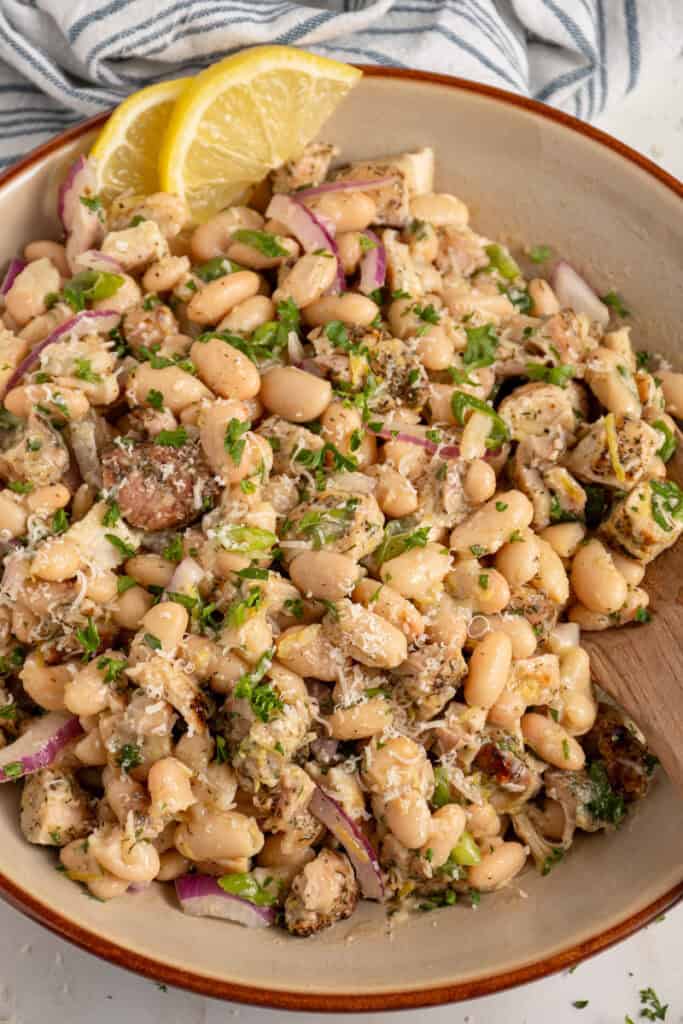 Bowl with dense white bean salad and grilled chicken garnished with parsley.