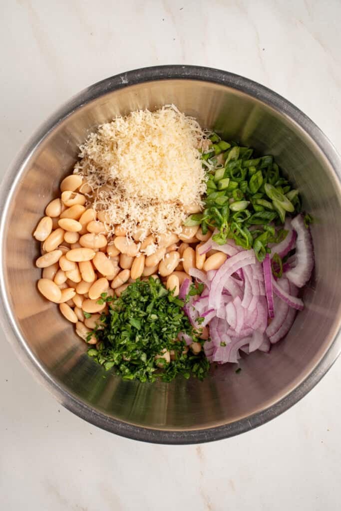 A bowl with ingredients for making dense white bean salad.