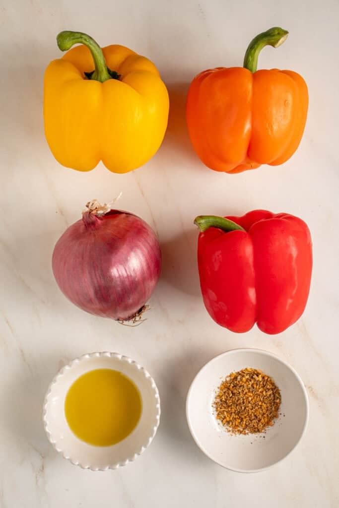 Ingredients for grilling peppers and onions laid out on a tabletop.