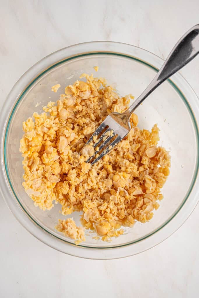 Smashed chickpeas with the back of a fork inside a bowl.