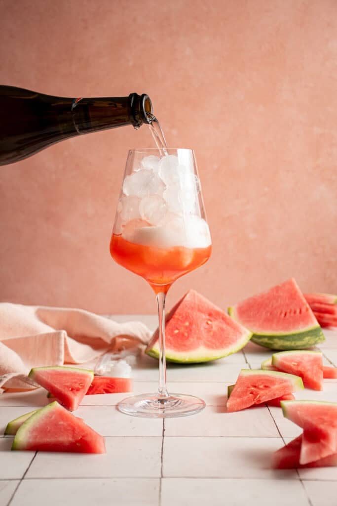 Pouring prosecco into a wine glass with ice.