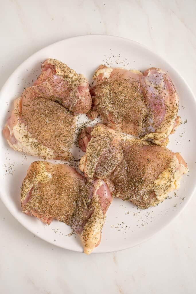 Seasoned raw chicken thighs on a plate.