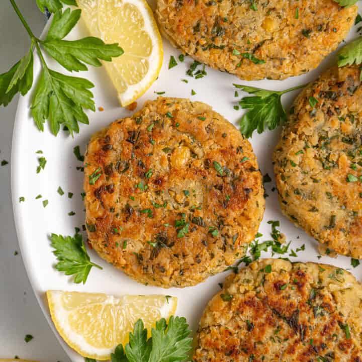 A plate with golden brown and crispy chickpea fritters, fresh parsley, and lemon slices.