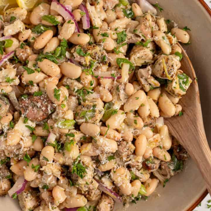 Bowl with dense white bean salad and grilled chicken garnished with parsley.