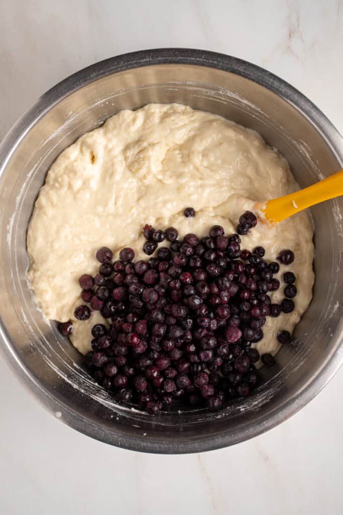 Pancake batter in a bowl with frozen wild blueberries.