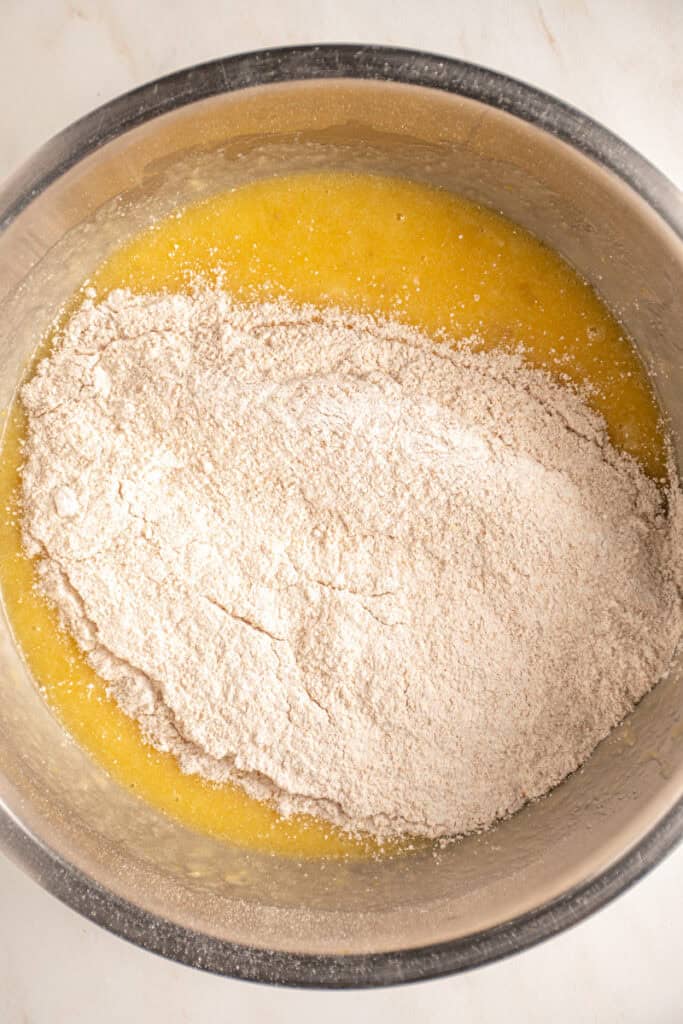Adding the dry ingredients to the wet ingredients for whole wheat banana muffins.