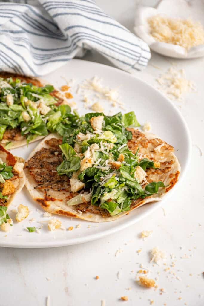 A plate with a smash chicken taco topped with chopped caesar salad with parmesan and crushed croutons.