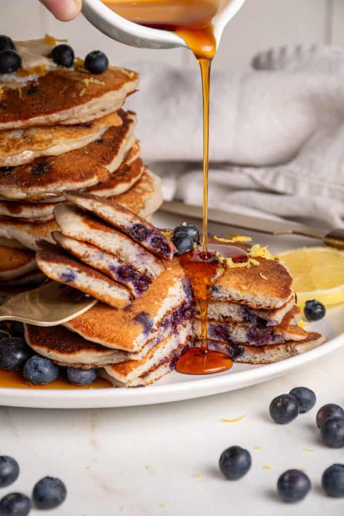Syrup being poured on a cut small stack of lemon blueberry pancakes.