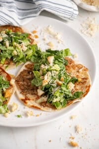 A plate with a smash chicken taco topped with chopped caesar salad with parmesan and crushed croutons.