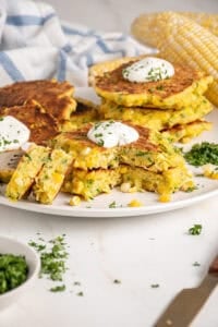 A stack of corn and zucchini fritters with a dollop of sour cream on top.