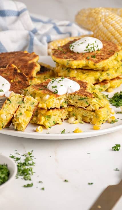 A stack of corn and zucchini fritters with a dollop of sour cream on top.
