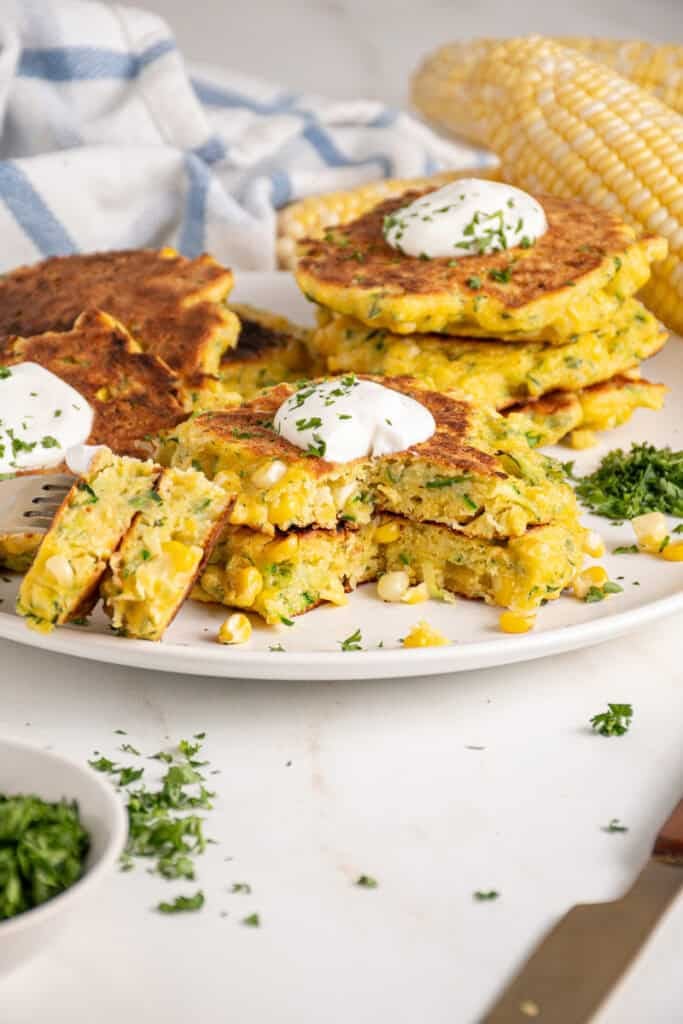 A stack of corn and zucchini fritters with a dollop of sour cream on top.